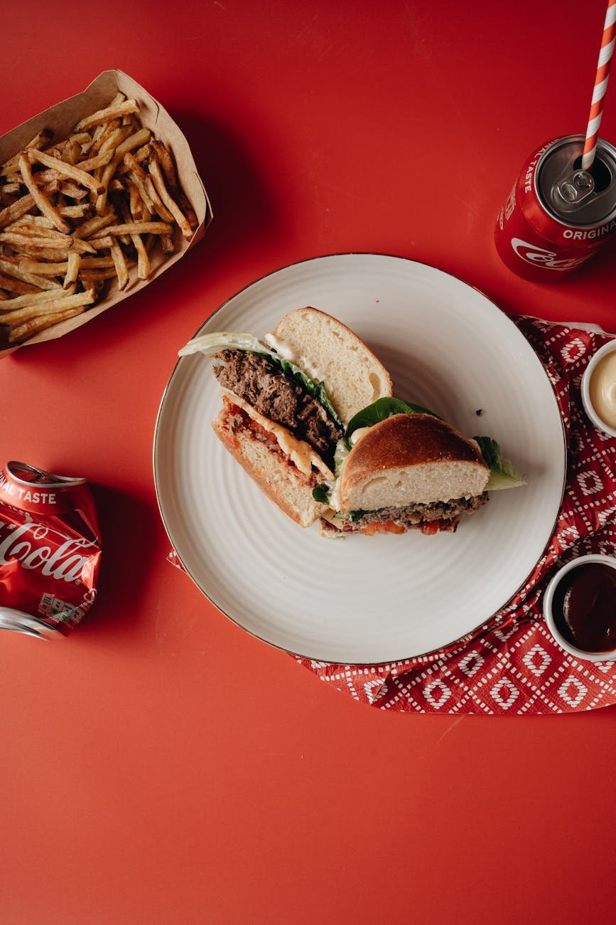 burger on white ceramic plate beside fries and soda